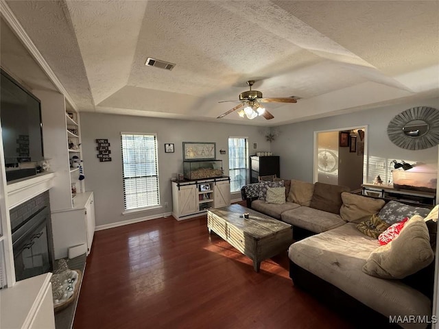 living room with dark wood-type flooring, ceiling fan, a tray ceiling, and a textured ceiling