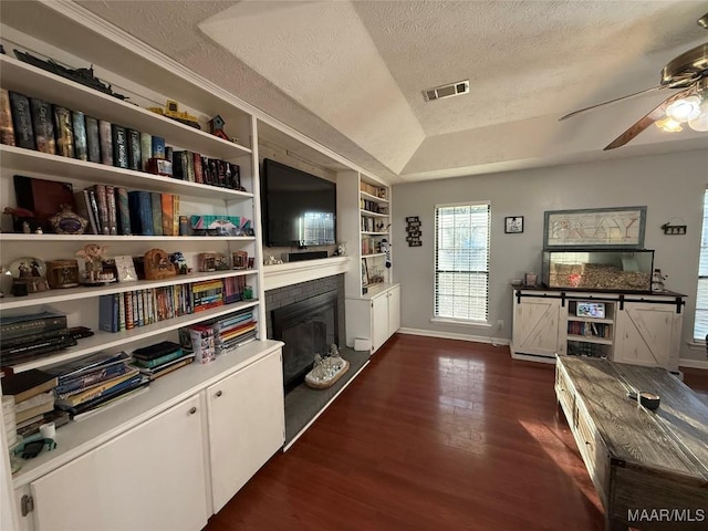 interior space with built in shelves, ceiling fan, dark hardwood / wood-style floors, and a textured ceiling