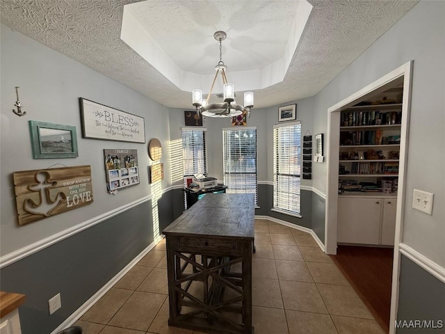 tiled dining room with an inviting chandelier, built in shelves, a raised ceiling, and a textured ceiling