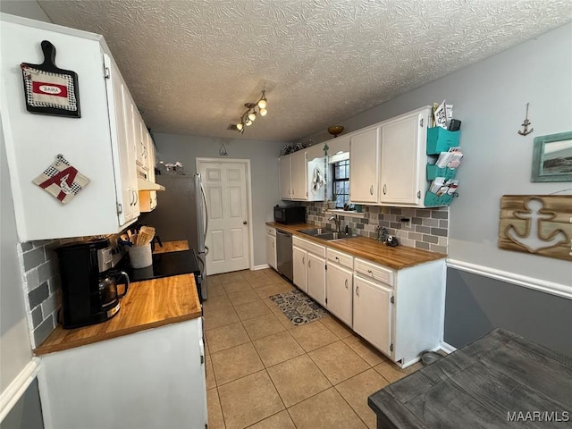 kitchen with light tile patterned flooring, sink, stainless steel appliances, decorative backsplash, and white cabinets