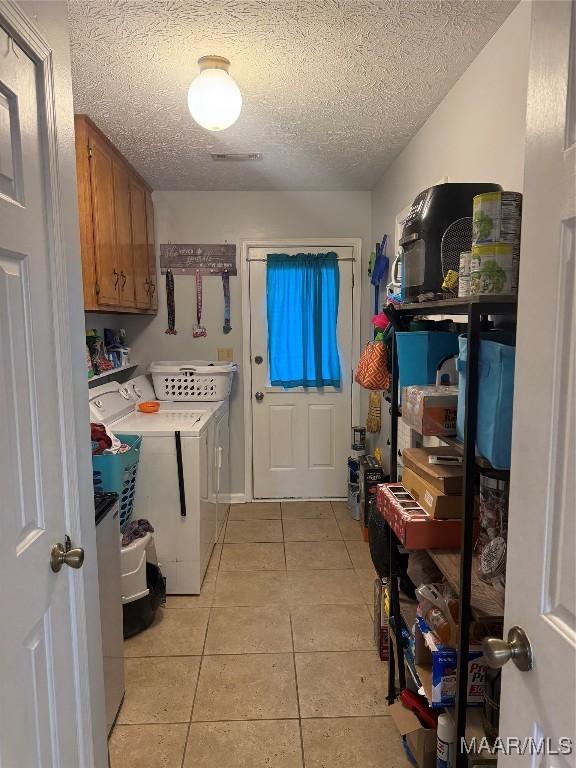 laundry room featuring cabinets, washing machine and dryer, a textured ceiling, and light tile patterned floors