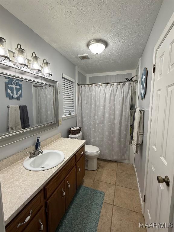 bathroom with curtained shower, tile patterned flooring, vanity, toilet, and a textured ceiling