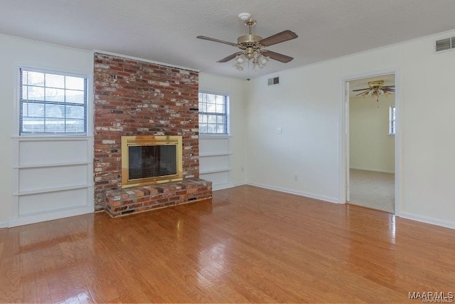 unfurnished living room featuring ceiling fan, a fireplace, light hardwood / wood-style flooring, and a textured ceiling