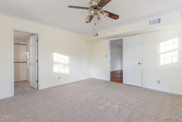 unfurnished bedroom featuring crown molding, a spacious closet, light colored carpet, and ceiling fan