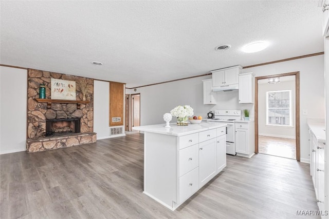 kitchen featuring a stone fireplace, a center island, white electric range, and white cabinets