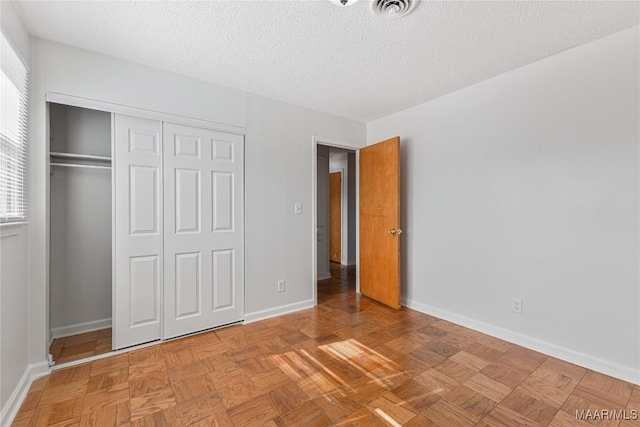 unfurnished bedroom featuring light parquet flooring, a textured ceiling, and a closet