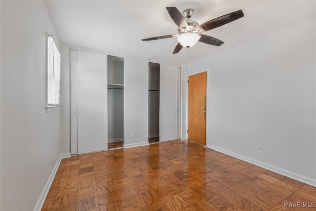 unfurnished bedroom with ceiling fan, parquet flooring, two closets, and a textured ceiling