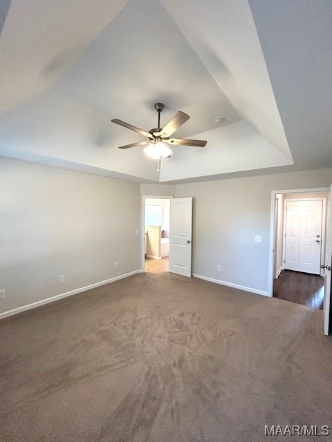 empty room with a raised ceiling, dark colored carpet, and ceiling fan