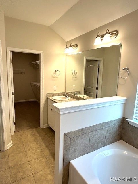 bathroom with lofted ceiling, vanity, tile patterned flooring, and a bathing tub