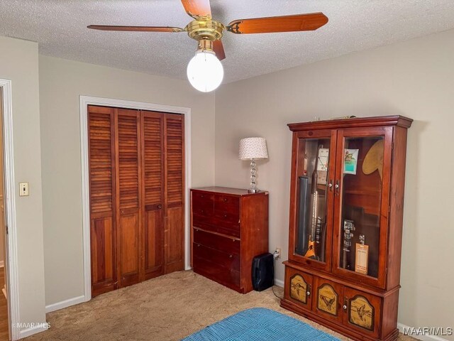 bedroom featuring ceiling fan, light carpet, a textured ceiling, and a closet