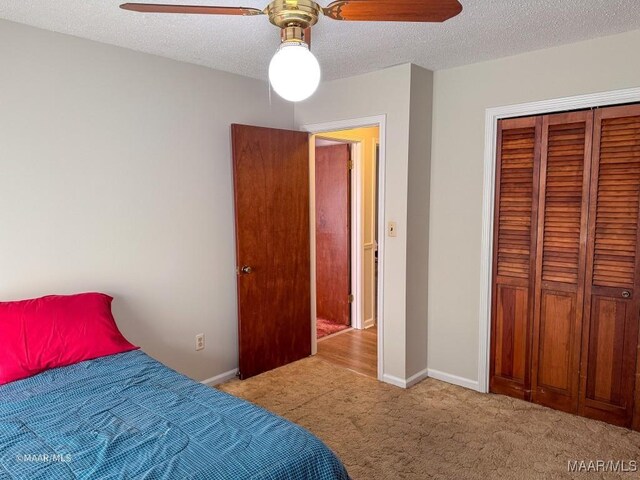 bedroom featuring ceiling fan, a closet, light carpet, and a textured ceiling