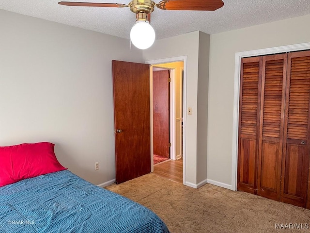 bedroom featuring light carpet, ceiling fan, a closet, and a textured ceiling