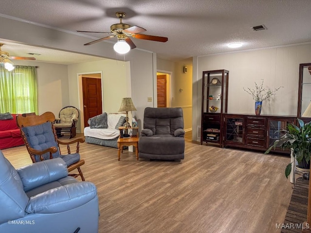 living room featuring crown molding, ceiling fan, wood-type flooring, and a textured ceiling