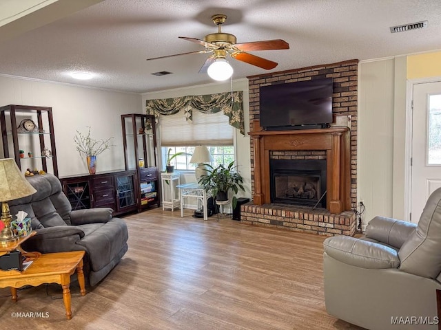 living room with crown molding, a brick fireplace, a textured ceiling, and light hardwood / wood-style floors