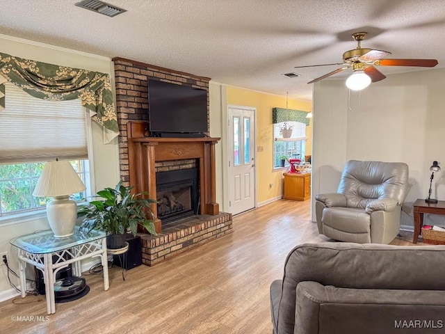 living room featuring ceiling fan, a fireplace, a textured ceiling, and light wood-type flooring