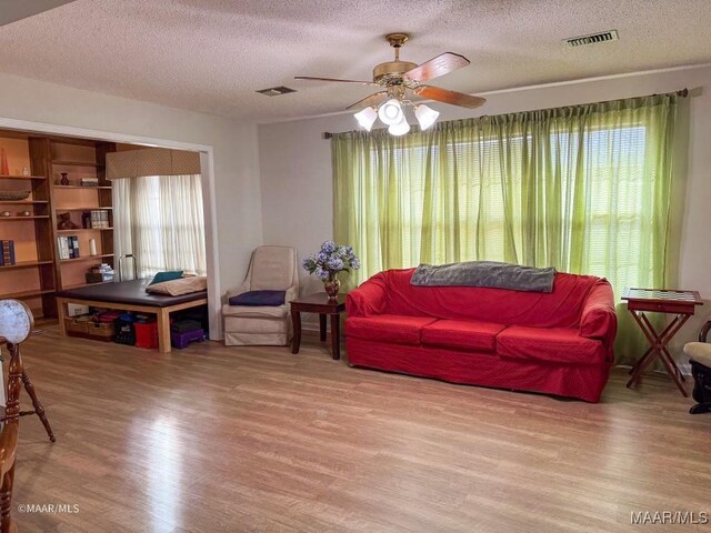 living room featuring ceiling fan, a textured ceiling, and light hardwood / wood-style flooring