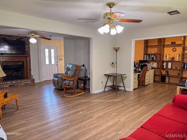 living room with a brick fireplace, wood-type flooring, and a textured ceiling