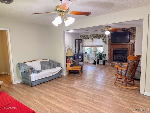 sitting room featuring a fireplace, light hardwood / wood-style flooring, a textured ceiling, and ceiling fan