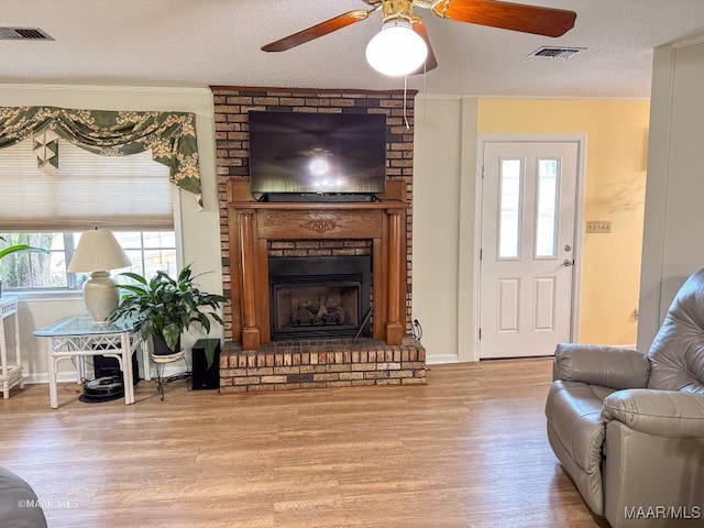 living room with a brick fireplace, ceiling fan, a textured ceiling, and light wood-type flooring