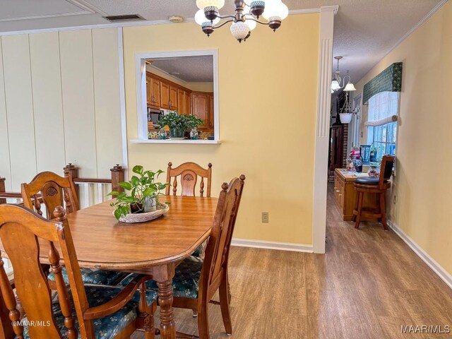 dining area featuring ornamental molding, light hardwood / wood-style floors, a textured ceiling, and a notable chandelier