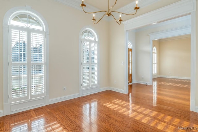 empty room with ornamental molding, an inviting chandelier, and light hardwood / wood-style flooring