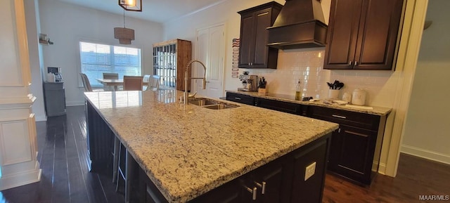 kitchen with sink, decorative light fixtures, a center island with sink, custom range hood, and light stone countertops