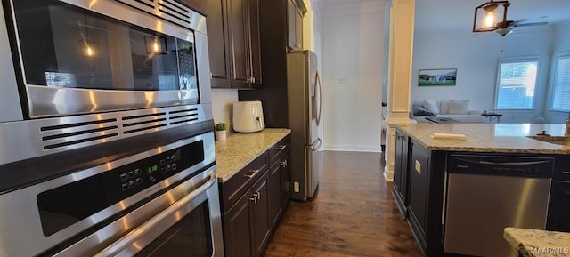 kitchen with light stone counters, dark brown cabinets, dark hardwood / wood-style floors, and appliances with stainless steel finishes