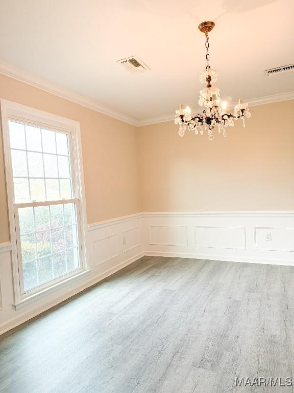 empty room with crown molding, wood-type flooring, and an inviting chandelier