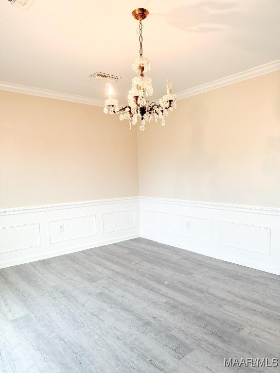 unfurnished room with hardwood / wood-style flooring, crown molding, and a chandelier