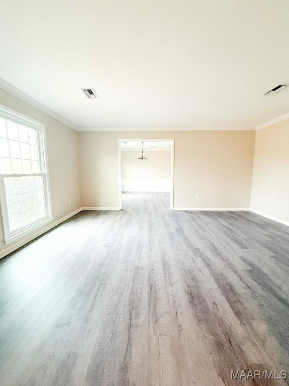 empty room with an inviting chandelier, crown molding, and wood-type flooring