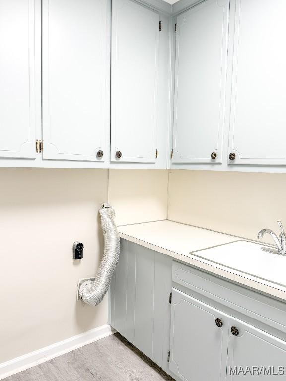 laundry room featuring sink, light hardwood / wood-style flooring, and cabinets