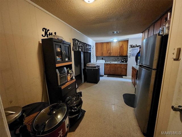 kitchen featuring stainless steel fridge, washer / dryer, a textured ceiling, and wood walls