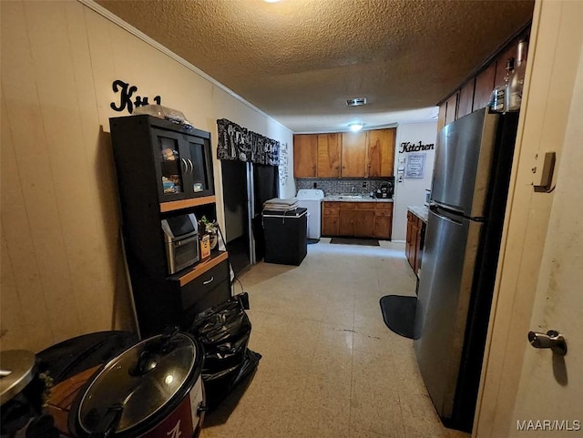 kitchen with sink, a textured ceiling, wooden walls, stainless steel fridge, and washer / clothes dryer