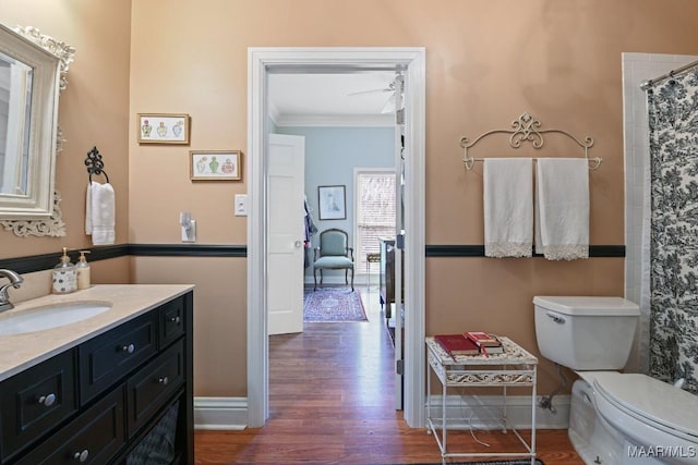 bathroom with ceiling fan, vanity, wood-type flooring, ornamental molding, and toilet