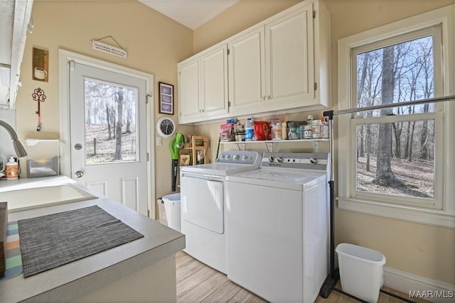 clothes washing area featuring sink, washer and clothes dryer, light hardwood / wood-style floors, and cabinets