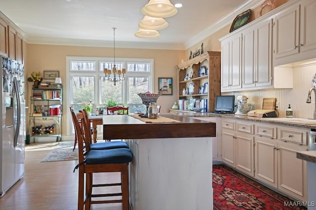 kitchen with dark wood-type flooring, crown molding, decorative light fixtures, stainless steel fridge, and a kitchen island