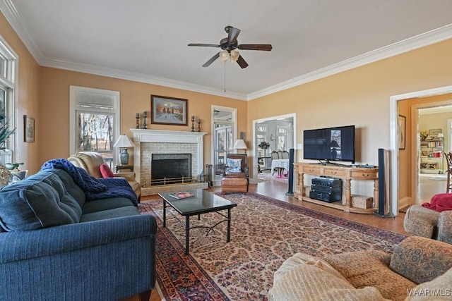 living room with a brick fireplace, wood-type flooring, ornamental molding, and ceiling fan