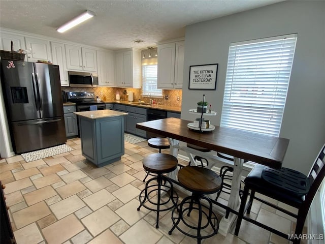 kitchen featuring sink, backsplash, stainless steel appliances, white cabinets, and a kitchen island