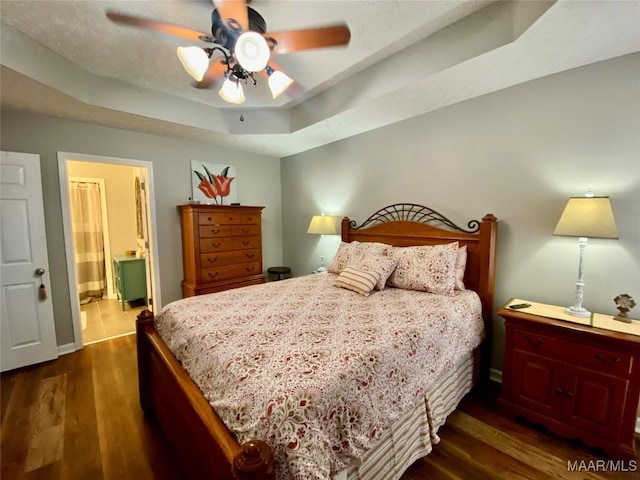 bedroom featuring a raised ceiling, dark hardwood / wood-style floors, connected bathroom, and ceiling fan