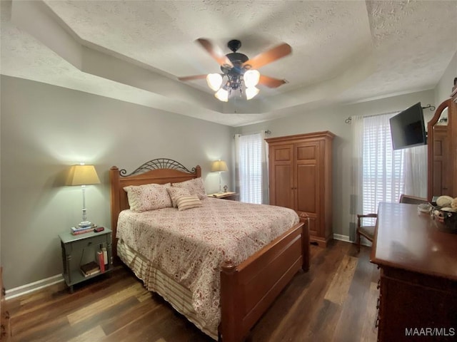 bedroom featuring a raised ceiling, dark wood-type flooring, a textured ceiling, and multiple windows