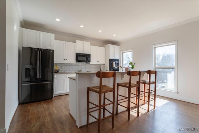 kitchen featuring white cabinetry, a breakfast bar area, black appliances, and a center island with sink