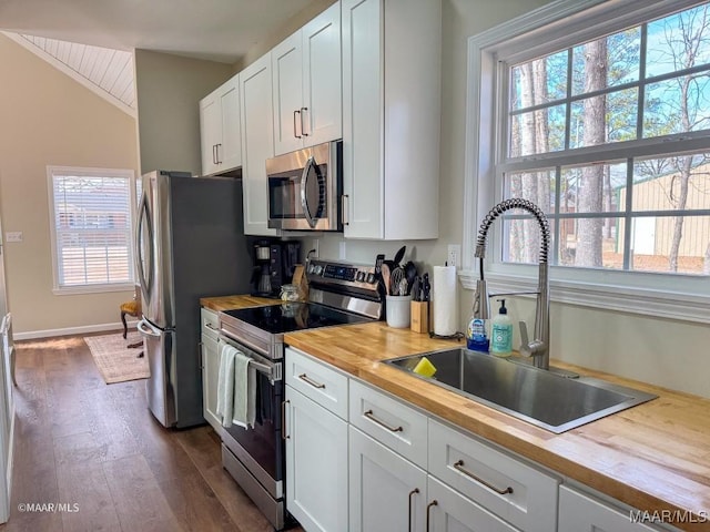 kitchen featuring stainless steel appliances, butcher block counters, sink, and white cabinets