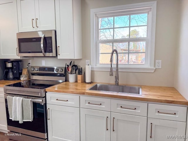 kitchen with wood counters, appliances with stainless steel finishes, sink, and white cabinets