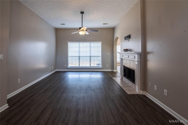 unfurnished living room featuring a tiled fireplace, ceiling fan, dark hardwood / wood-style floors, and a textured ceiling