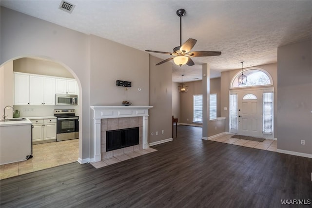 unfurnished living room with sink, a tile fireplace, ceiling fan, light hardwood / wood-style floors, and a textured ceiling