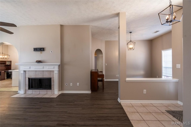 unfurnished living room featuring hardwood / wood-style flooring, a fireplace, ceiling fan with notable chandelier, and a textured ceiling