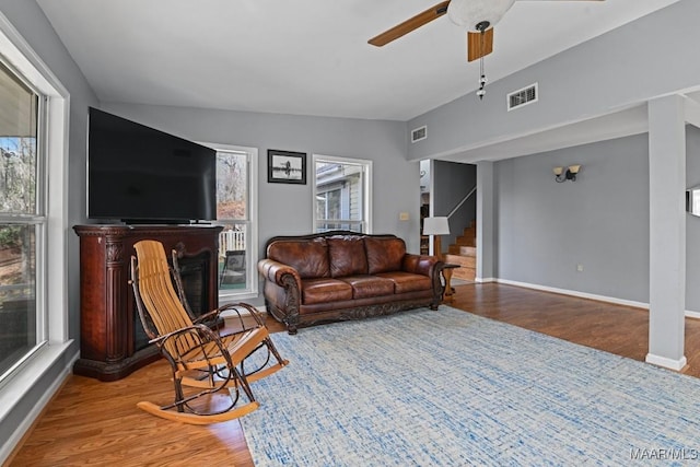 living room featuring a fireplace, wood finished floors, visible vents, vaulted ceiling, and stairs