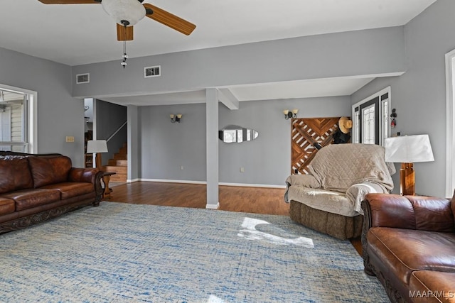 living area featuring wood finished floors, visible vents, ceiling fan, and stairs