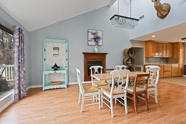 dining room with high vaulted ceiling, light wood finished floors, a fireplace, and baseboards