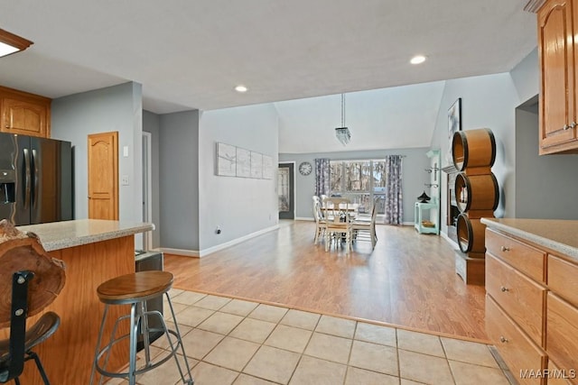 kitchen featuring light tile patterned flooring, light countertops, fridge with ice dispenser, hanging light fixtures, and a kitchen bar